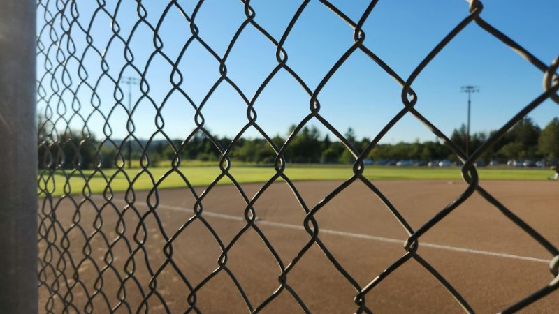 A softball field seen through a chain-link fence on a sunny day