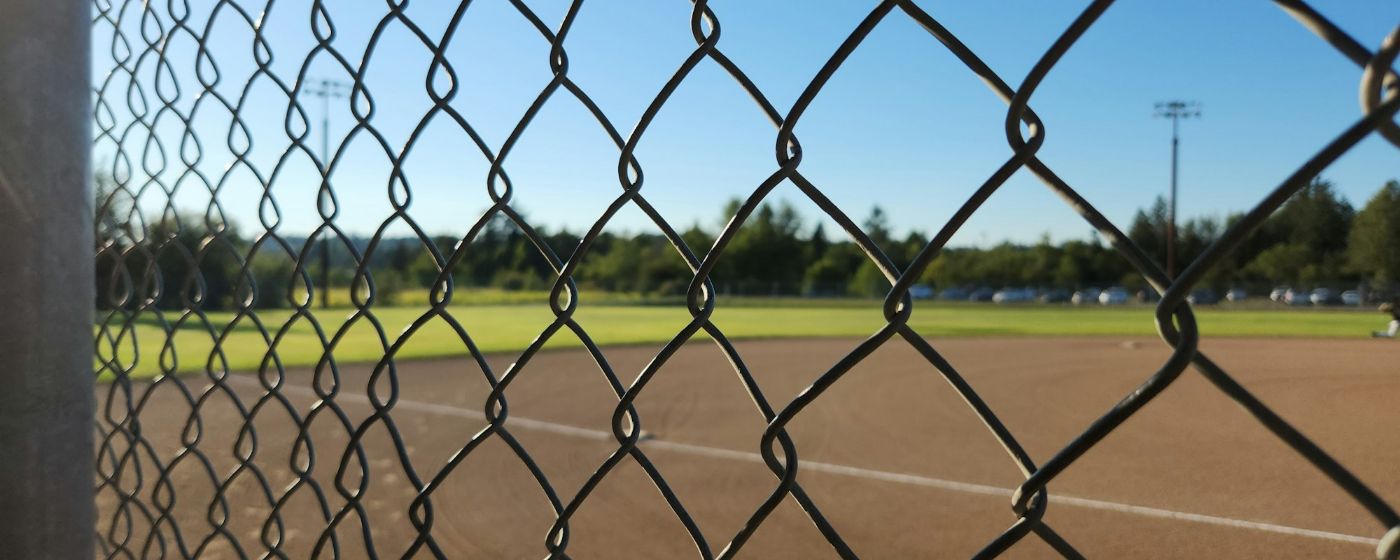 A softball field seen through a chain-link fence on a sunny day